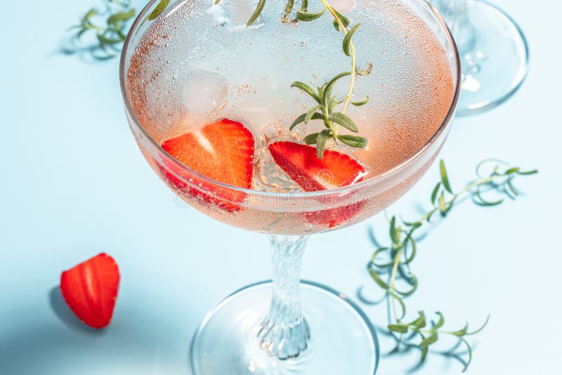 Glass of strawberry cocktail or mocktail, refreshing summer drink with champagne, strawberries, ice cubes and rosemary on blue