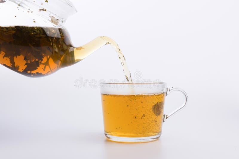 Glass teapot pouring green tea into cup isolated on white background