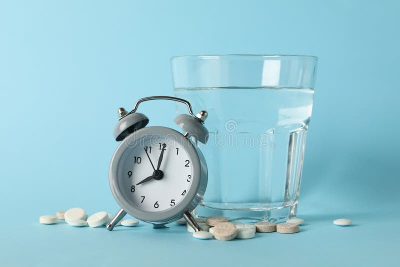 Glass of Water, Alarm Clock and Pills on Blue Background Stock Image