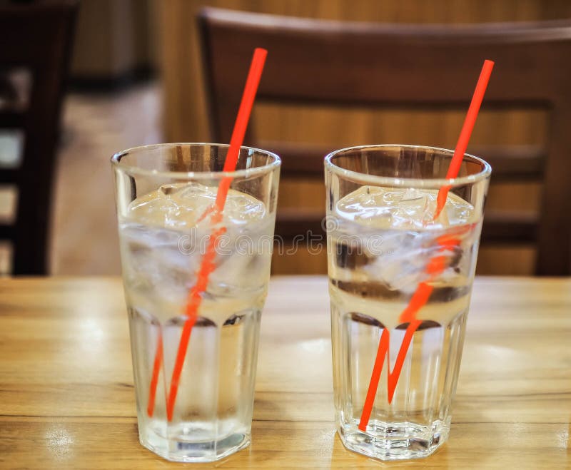 Glass of water with red straw on wooden table