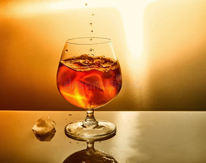 Glass of whiskey with drops and ice on an orange background stock photography Glass of whiskey with drops and ice on an orange background stock photography