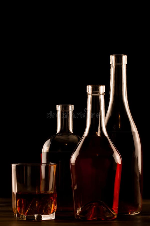 Glass of whiskey with ice and a bottle on a wooden table.