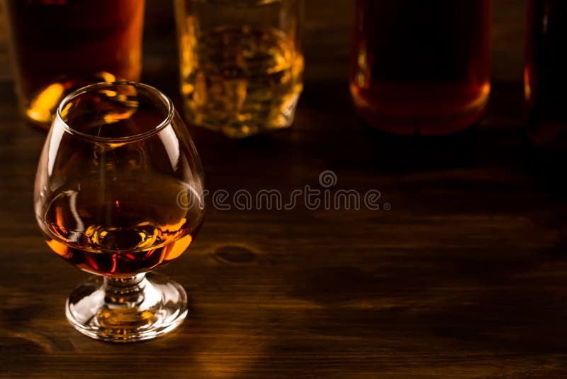 Glass of whiskey with ice and a bottle on a wooden table.