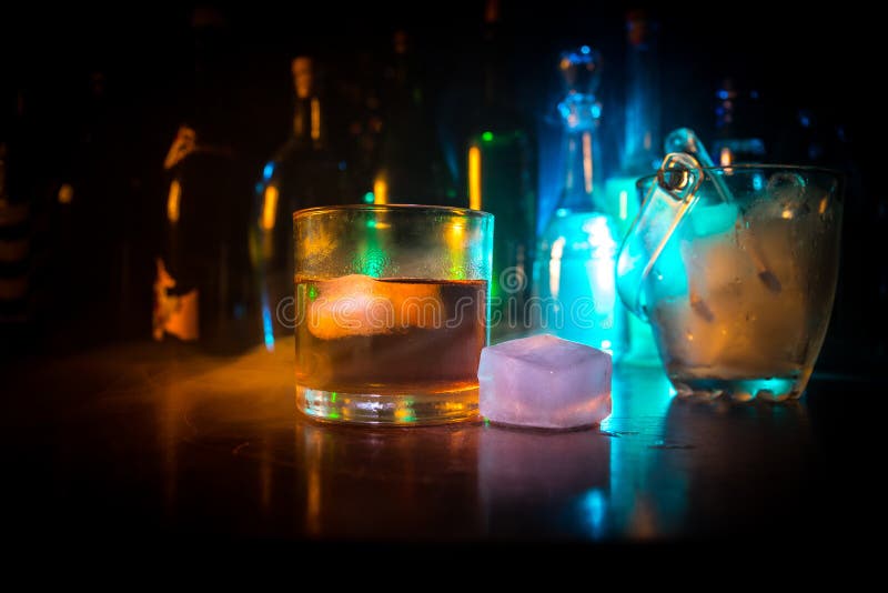 Glass of whisky on wooden bar closeup with bottles blurred view on dark background with light and smoke. Single glass of whisky on royalty free stock photo Glass of whisky on wooden bar closeup with bottles blurred view on dark background with light and smoke. Single glass of whisky on royalty free stock photo