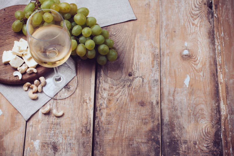 Ein Glas weißen Wein, Trauben, cashew-Nüssen und weichem Käse auf einem holzbrett, Landhausstil hintergrund.