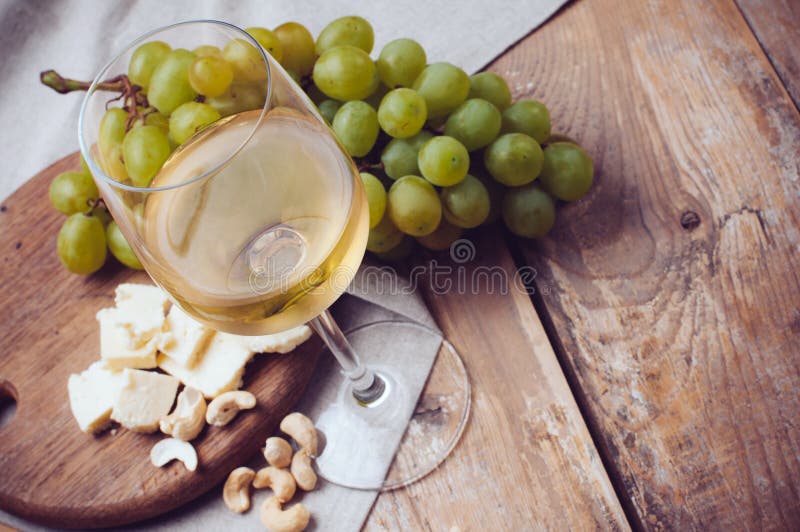 Glass of white wine, grapes, cashew nuts and soft cheese