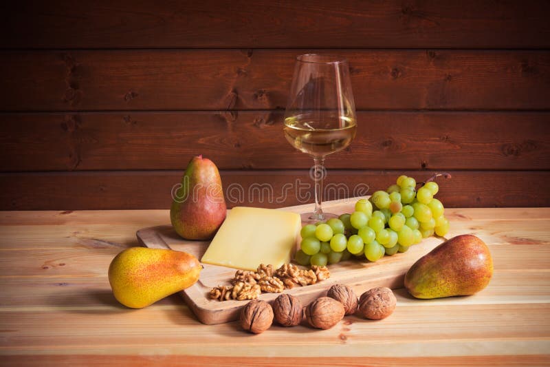 Glass of white wine, parmesan cheese, walnuts, pears  and grape branch on wooden table