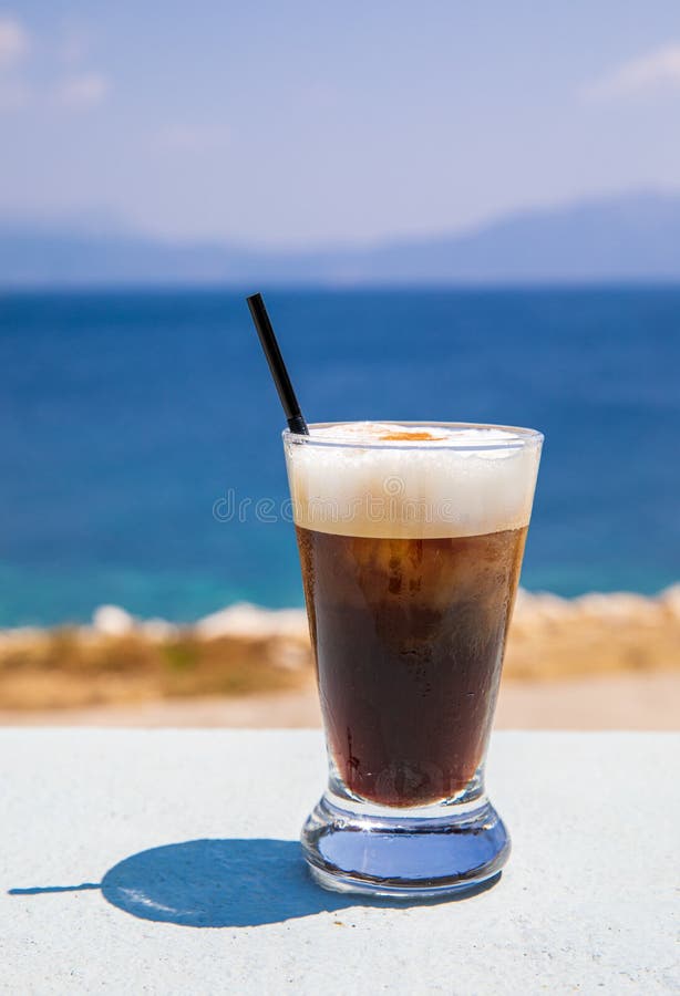 Glass of yummy iced coffee or greek freddo cappuccino on the seascape background on a summer sunny day in Kastos island