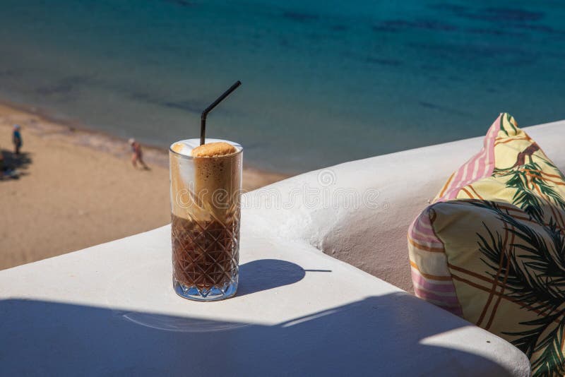 Glass of yummy iced coffee or greek freddo cappuccino on the seascape background on a summer sunny day at the Kythnos