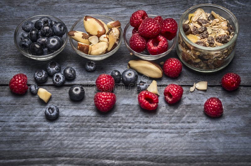 Glasschüsseln mit Bestandteilen zum gesundes Frühstück - muesli, Beeren und Nüsse auf blauem rustikalem hölzernem Hintergrund