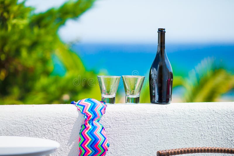 Glasses, bottle of tasty wine and swimsuit on balcony in greek island with view of sea.