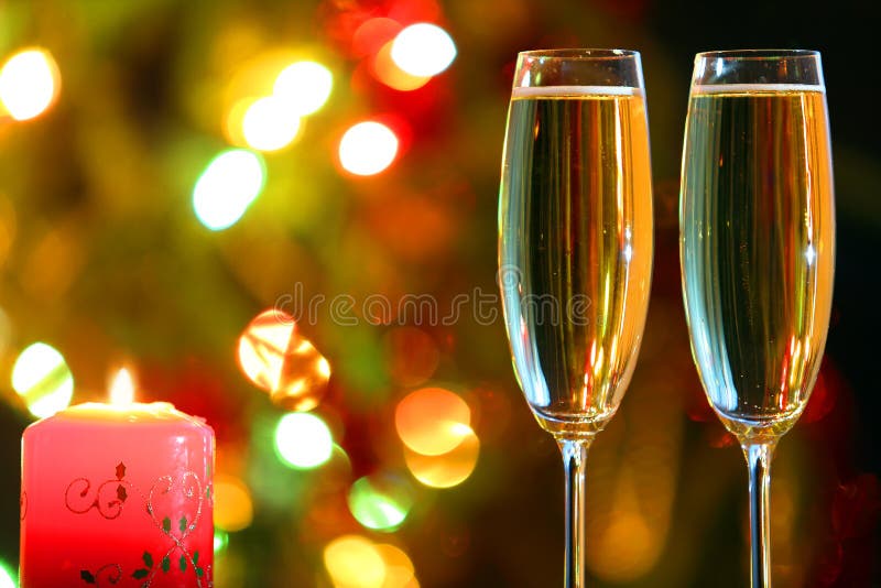 Glasses with champagne and candle against festive lights