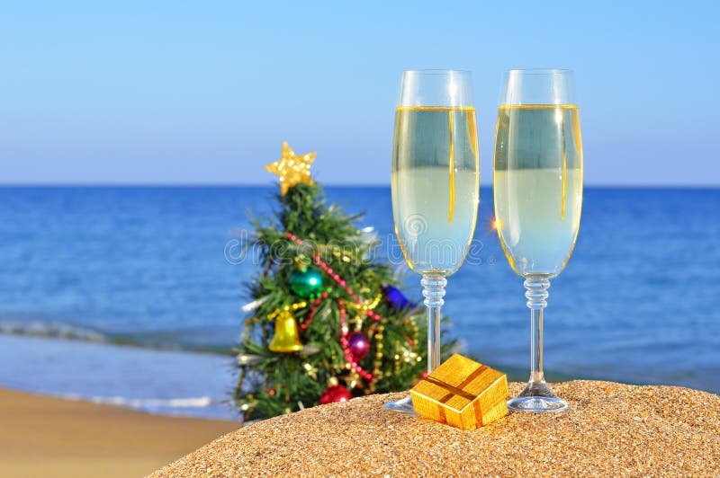Glasses of champagne and Christmas tree on a beach