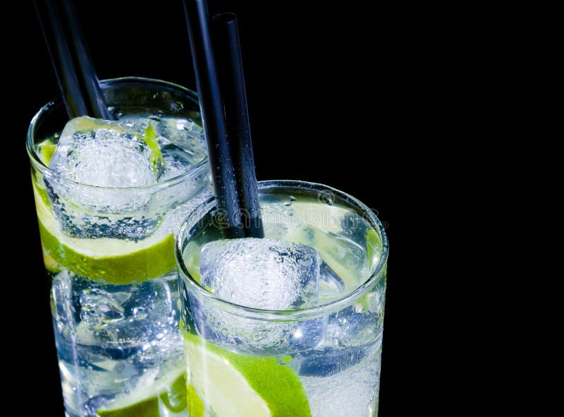 Glasses with cocktail and ice with lime slice on black background with space for text