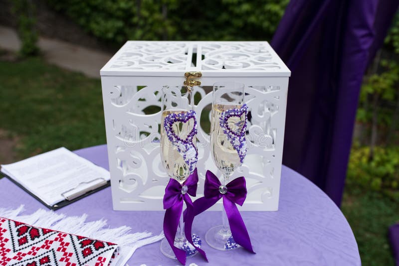 Glasses with lilac hearts and ribbons of bride and groom with champagne are standing before the white wooden boxes in wedding cere stock images Glasses with lilac hearts and ribbons of bride and groom with champagne are standing before the white wooden boxes in wedding cere stock images