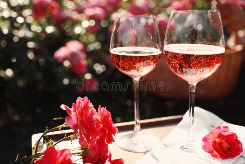 Glasses of rose wine on table in blooming garden