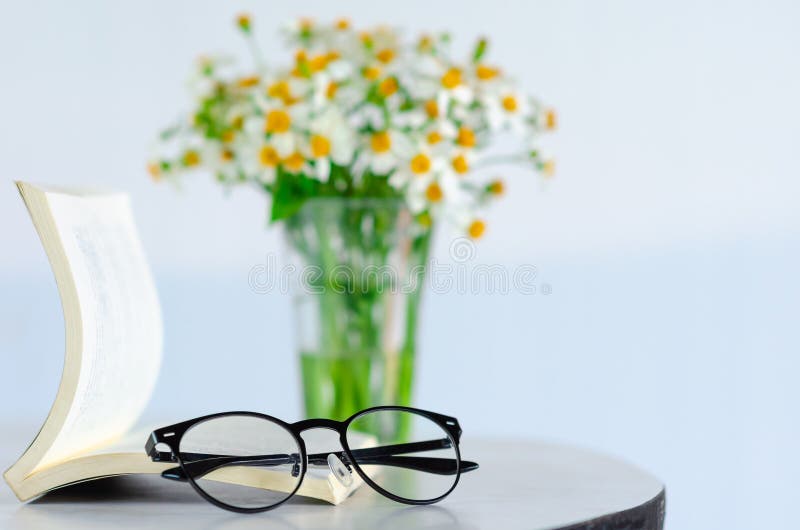 Spectacles puts on a book with blurred flowers background. Spectacles puts on a book with blurred flowers background