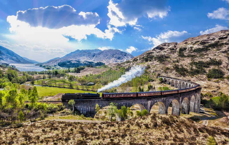 Glenfinnan Railway Viaduct in Scotland with the Jacobite steam train against sunset over lake. Famous Glenfinnan Railway Viaduct in Scotland with the Jacobite stock photography Glenfinnan Railway Viaduct in Scotland with the Jacobite steam train against sunset over lake. Famous Glenfinnan Railway Viaduct in Scotland with the Jacobite stock photography