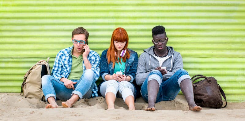 Multiracial friends using mobile smart phone at beach on relax moment - Young bored people addicted by smartphone - Technology concept with always connected millennials. Multiracial friends using mobile smart phone at beach on relax moment - Young bored people addicted by smartphone - Technology concept with always connected millennials