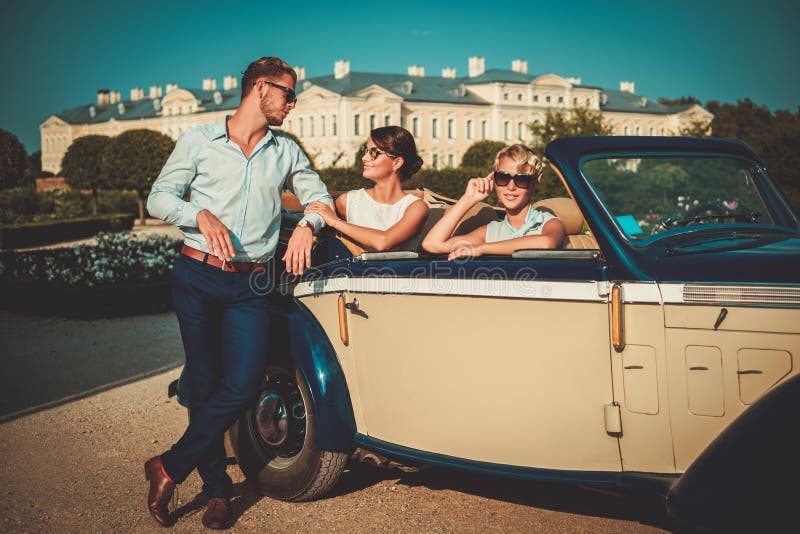 Gli amici ricchi si avvicinano al convertibile classico fotografie stock libere da diritti Gli amici ricchi si avvicinano al convertibile classico fotografie stock libere da diritti