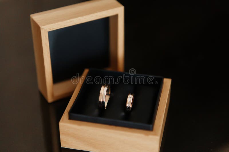 Gli anelli delle nozze d'oro giacciono in una scatola di regali di legno su un tavolo nero di vetro immagine stock libera da diritti