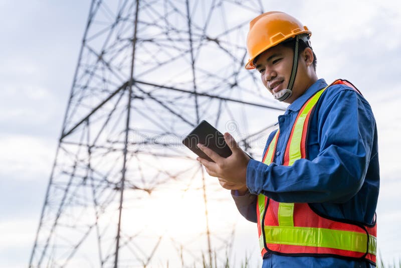 Gli ingegneri elettrici asiatici indossano abiti di sicurezza in piedi e guardano la centrale elettrica per vedere il lavoro di p fotografie stock Gli ingegneri elettrici asiatici indossano abiti di sicurezza in piedi e guardano la centrale elettrica per vedere il lavoro di p fotografie stock
