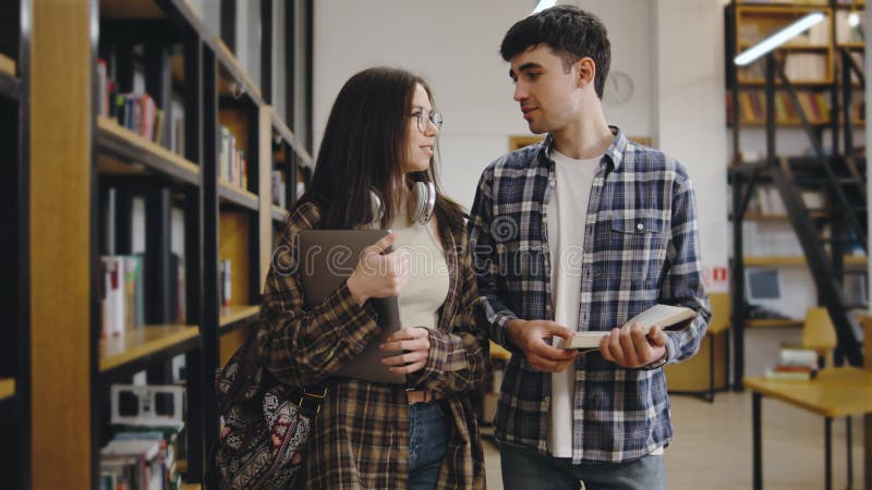 Gli studenti esplorano una biblioteca mentre discutono scelte di libri e argomenti di ricerca durante una tranquilla sessione pome video d archivio