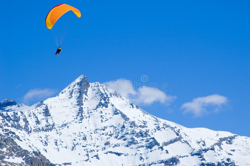 An orange glider circling above snowed mountains. An orange glider circling above snowed mountains