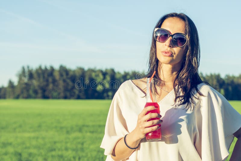 Glimlachen het Youn slanke meisje met glazen en het krullende haar en drinken een alcoholische of niet-alkoholische rode cocktail stock afbeelding Glimlachen het Youn slanke meisje met glazen en het krullende haar en drinken een alcoholische of niet-alkoholische rode cocktail stock afbeelding
