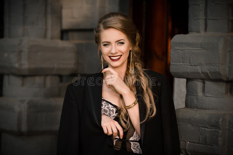 Glimlachend gelukkig vrolijk modieus meisje in zwarte kleding, jasje op de achtergrond van de muursteen Het concept van het geluk royalty-vrije stock foto Glimlachend gelukkig vrolijk modieus meisje in zwarte kleding, jasje op de achtergrond van de muursteen Het concept van het geluk royalty-vrije stock foto
