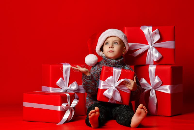 Glimlachend grappig kind in gift van de holdingskerstmis van de Kerstman de rode hoed ter beschikking Kerstmistak en klokken royalty-vrije stock afbeeldingen Glimlachend grappig kind in gift van de holdingskerstmis van de Kerstman de rode hoed ter beschikking Kerstmistak en klokken royalty-vrije stock afbeeldingen