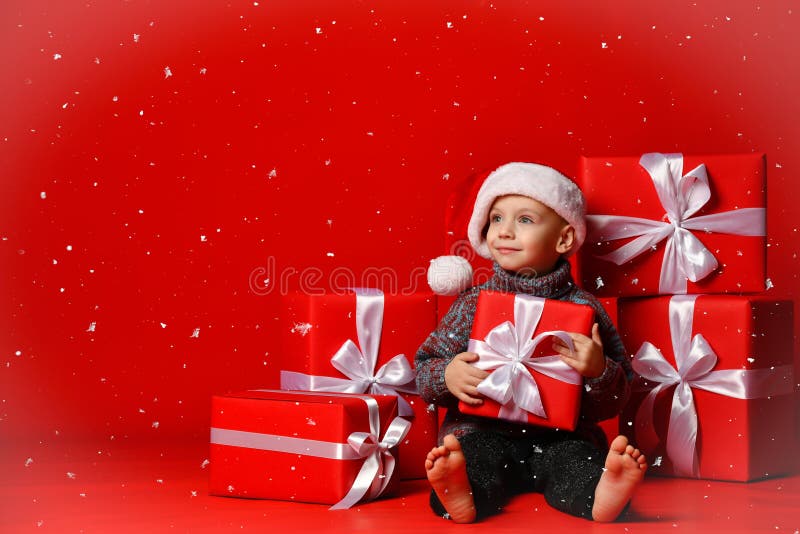 Glimlachend grappig kind in gift van de holdingskerstmis van de Kerstman de rode hoed ter beschikking Kerstmistak en klokken royalty-vrije stock afbeelding Glimlachend grappig kind in gift van de holdingskerstmis van de Kerstman de rode hoed ter beschikking Kerstmistak en klokken royalty-vrije stock afbeelding