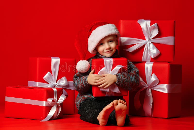 Glimlachend grappig kind in gift van de holdingskerstmis van de Kerstman de rode hoed ter beschikking Kerstmistak en klokken stock afbeelding Glimlachend grappig kind in gift van de holdingskerstmis van de Kerstman de rode hoed ter beschikking Kerstmistak en klokken stock afbeelding