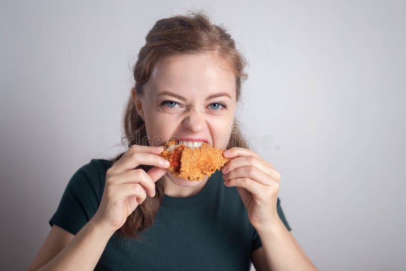 Glimlachend jong caucasiaans meisje dat gefrituurde kip met een drumstick eet