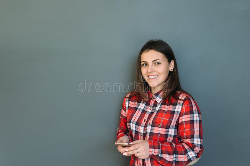 Glimlachend meisje die zich door muur en de telefoon in haar handen bevinden te houden stock foto Glimlachend meisje die zich door muur en de telefoon in haar handen bevinden te houden stock foto