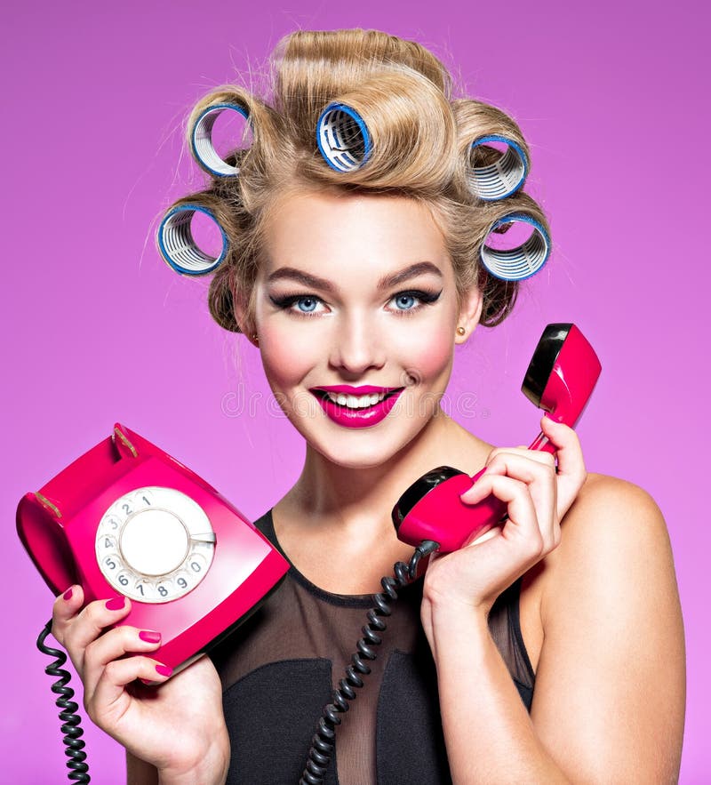 Smiling girl with blue curlers talking by red telephone. Young happy woman with blue curlers calling by retro phone. Portrain of an atractive female using a vintage phone. Smiling girl with blue curlers talking by red telephone. Young happy woman with blue curlers calling by retro phone. Portrain of an atractive female using a vintage phone
