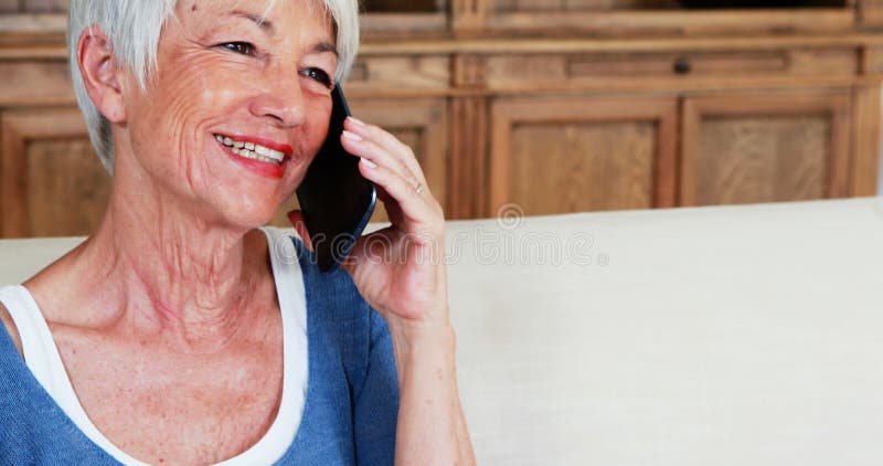 Glimlachende hogere vrouw die op mobiele telefoon in woonkamer spreken