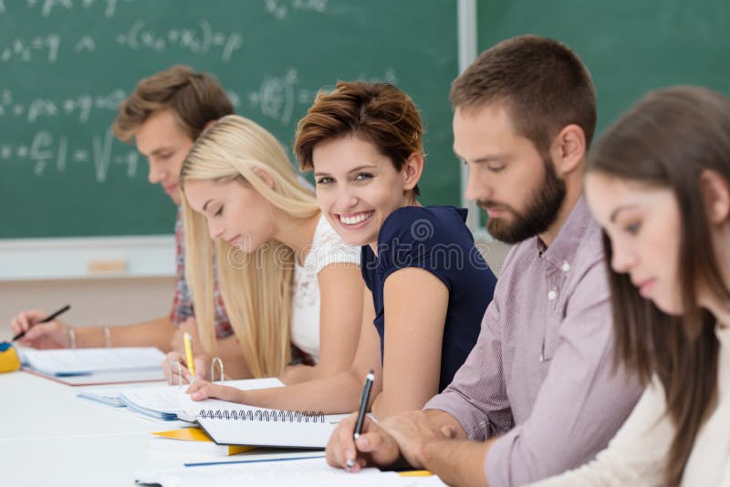 Smiling beautiful young women in the classroom sitting in a line of students working together at a long table, turning to smile at the camera. Smiling beautiful young women in the classroom sitting in a line of students working together at a long table, turning to smile at the camera