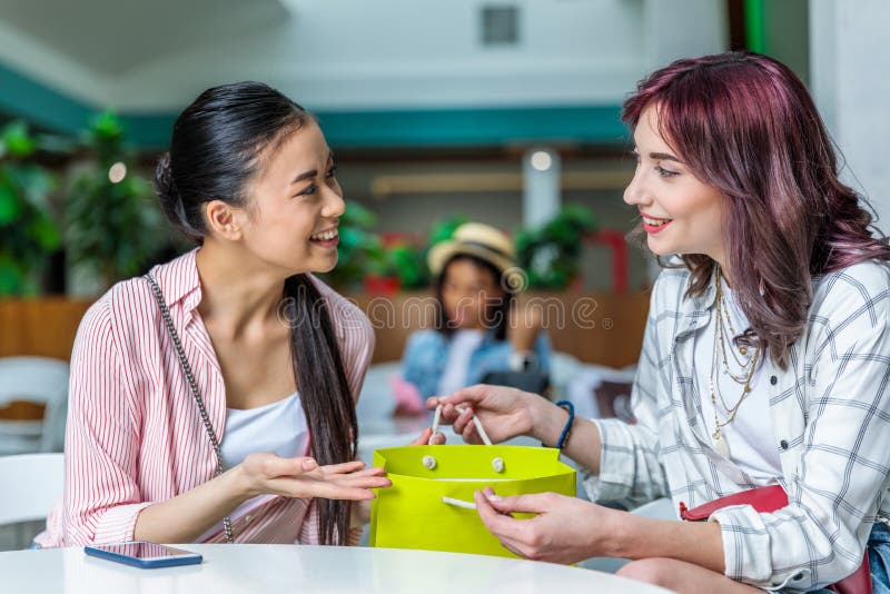 Glimlachende jonge vrouwen met het winkelen zakzitting samen en het spreken stock afbeelding Glimlachende jonge vrouwen met het winkelen zakzitting samen en het spreken stock afbeelding