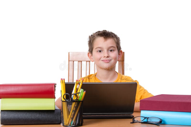 Smiling little boy at desk with laptop in between piles of large books and cup of pencils and pens. Smiling little boy at desk with laptop in between piles of large books and cup of pencils and pens