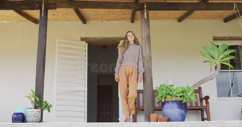 Glimlachende kaukasische vrouw die buiten huis leunt en uit terrace kijkt