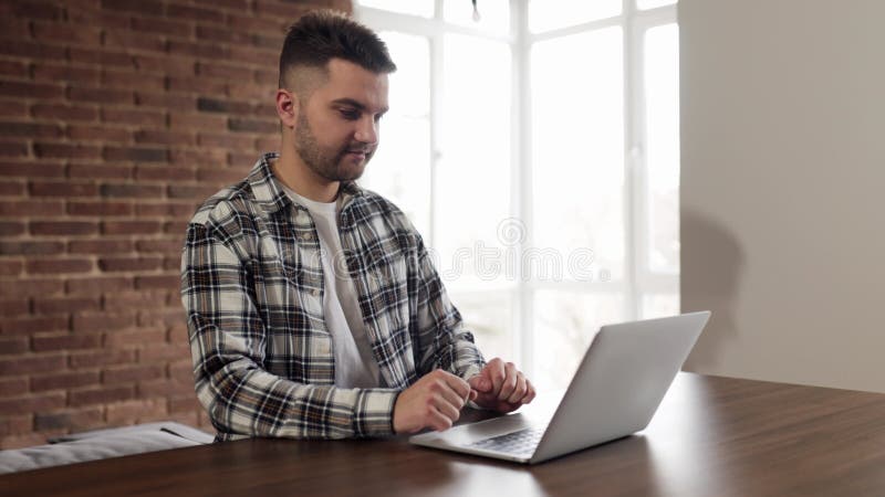 Glimlachende man gebruikt een laptop die sms't en geniet van vriendschappelijke communicatie thuis aan tafel. moderne technologie