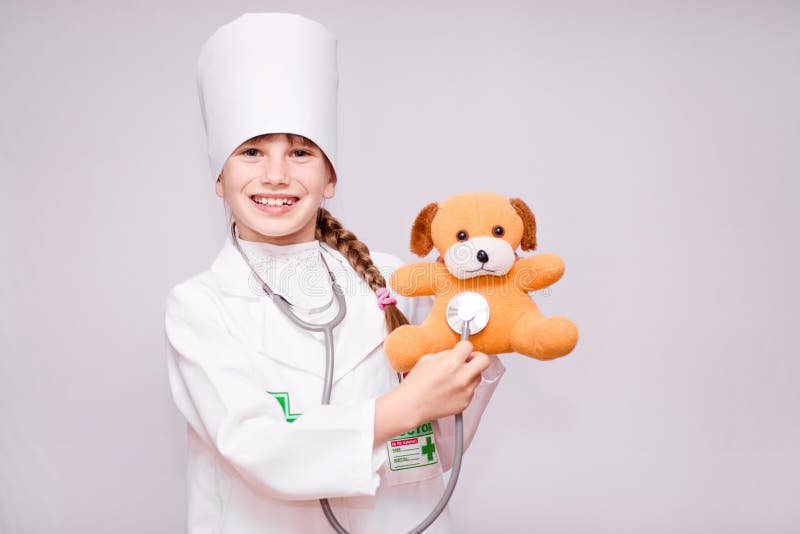 Glimlachende meisje speelarts en luisterteddybeer met stethoscoop op wit stock afbeelding Glimlachende meisje speelarts en luisterteddybeer met stethoscoop op wit stock afbeelding