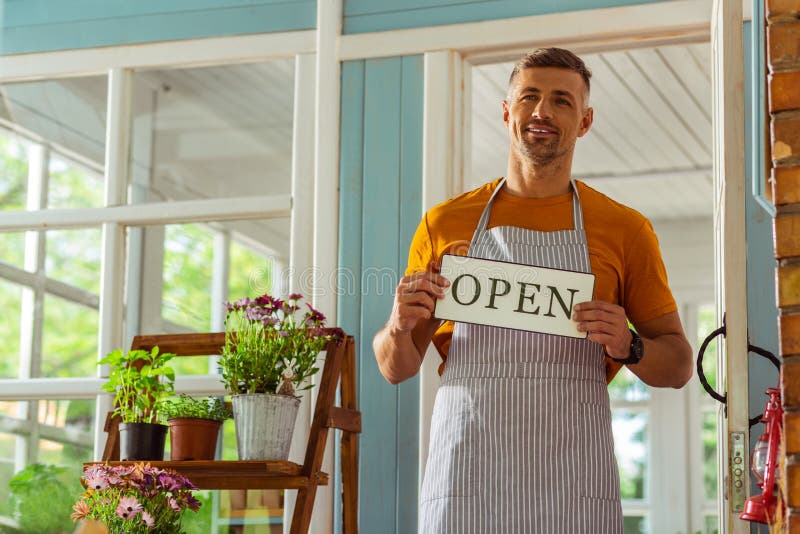 Glimlachende mens die een open teken houden dichtbij zijn winkel stock afbeeldingen Glimlachende mens die een open teken houden dichtbij zijn winkel stock afbeeldingen
