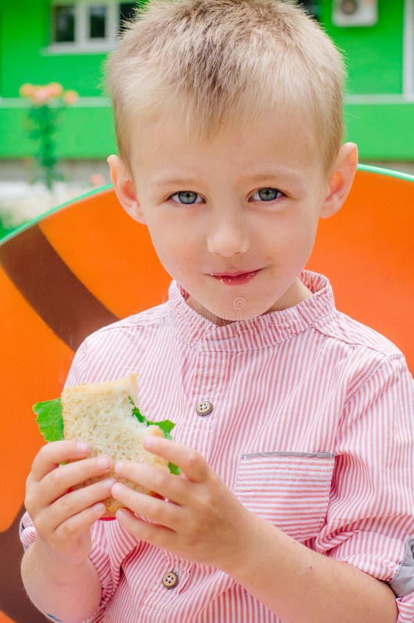 Glimlachende schooljongen die sandwichzitting eten dichtbij de basisschool royalty-vrije stock foto Glimlachende schooljongen die sandwichzitting eten dichtbij de basisschool royalty-vrije stock foto