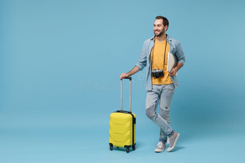 Smiling traveler tourist man in yellow clothes with photo camera isolated on blue background. Male passenger traveling abroad on weekend. Air flight journey concept. Hold suitcase laptop pc computer. Smiling traveler tourist man in yellow clothes with photo camera isolated on blue background. Male passenger traveling abroad on weekend. Air flight journey concept. Hold suitcase laptop pc computer