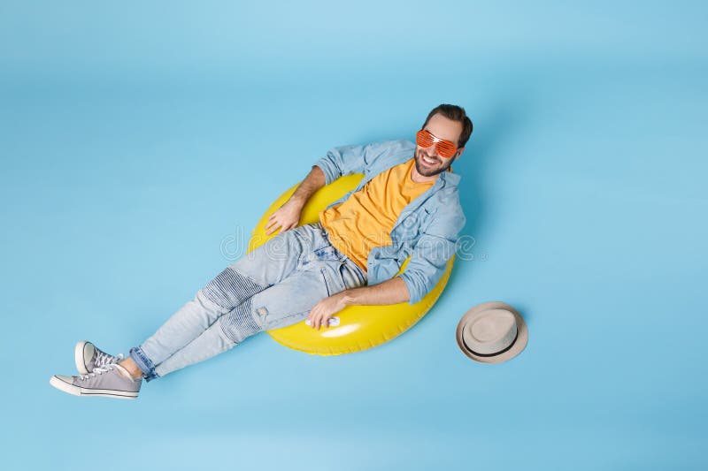 Smiling traveler tourist man in casual summer yellow clothes eyeglasses isolated on blue background. Passenger traveling abroad to travel on weekend. Air flight journey concept. Lying in rubber ring. Smiling traveler tourist man in casual summer yellow clothes eyeglasses isolated on blue background. Passenger traveling abroad to travel on weekend. Air flight journey concept. Lying in rubber ring