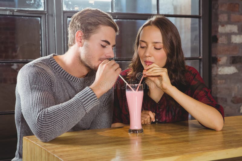 Glimlachende vrienden die smoothie en door stro drinken delen stock fotografie Glimlachende vrienden die smoothie en door stro drinken delen stock fotografie