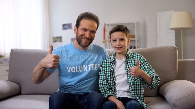 Glimlachende vrijwilliger en schooljongen die op middelbare leeftijd duim-omhoog aan camera, advertentie tonen stock foto's Glimlachende vrijwilliger en schooljongen die op middelbare leeftijd duim-omhoog aan camera, advertentie tonen stock foto's