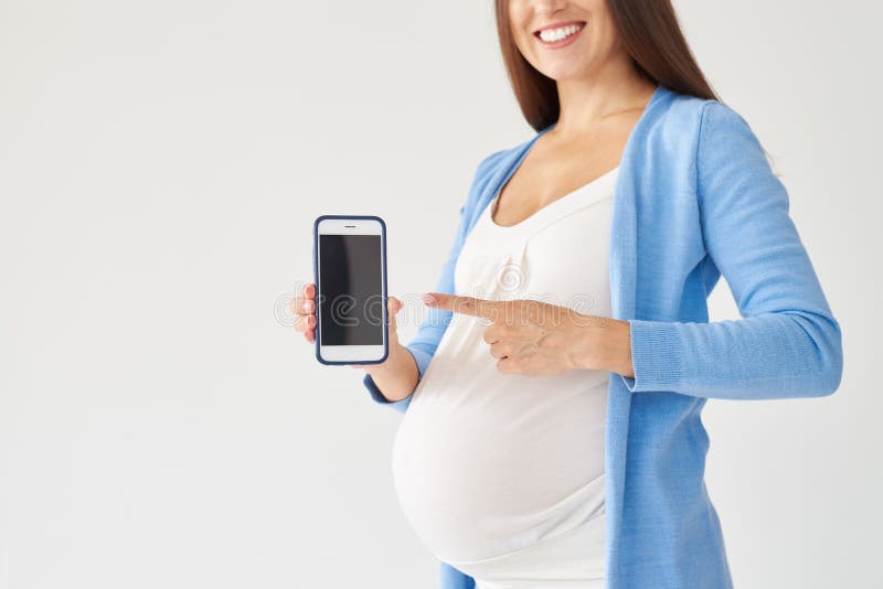 Glimlachende zwangere vrouw die op smartphone met het zwarte scherm richten stock fotografie Glimlachende zwangere vrouw die op smartphone met het zwarte scherm richten stock fotografie